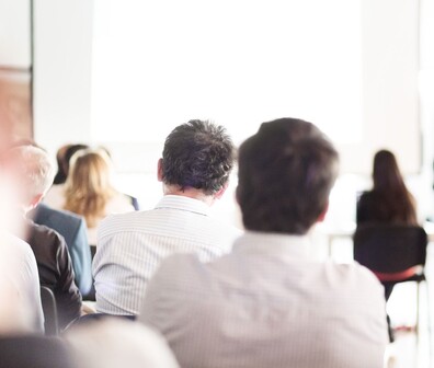 Quadratisches Bild von Personen die einem Vortrag zuhören