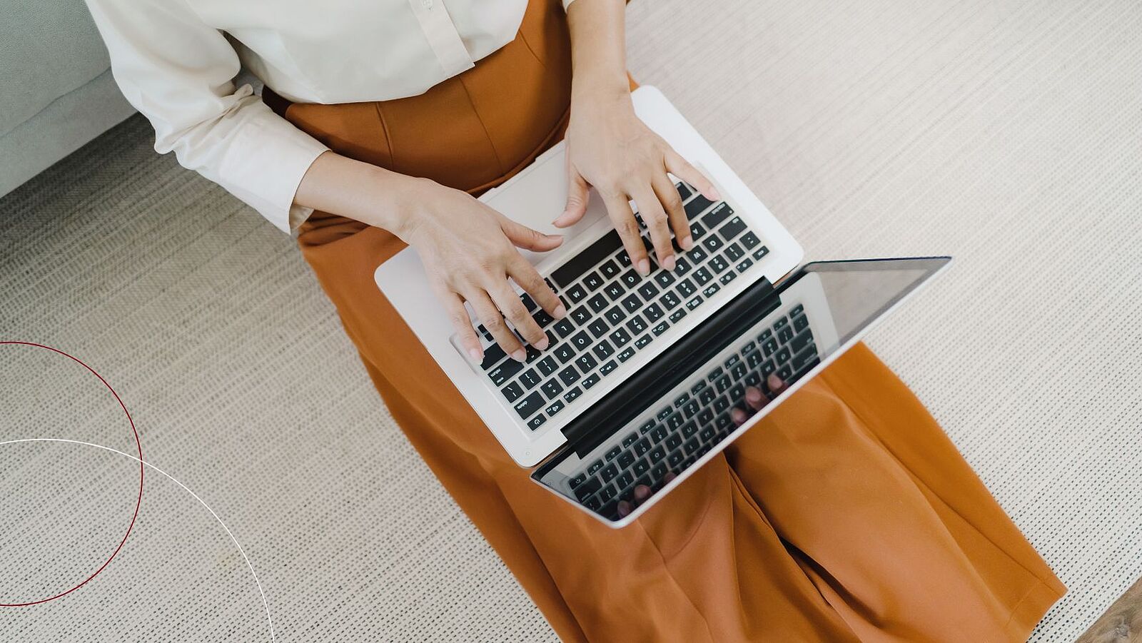 Frau sitzt auf dem Wohnzimmerfußboden mit einem Laptop auf den Beinen.