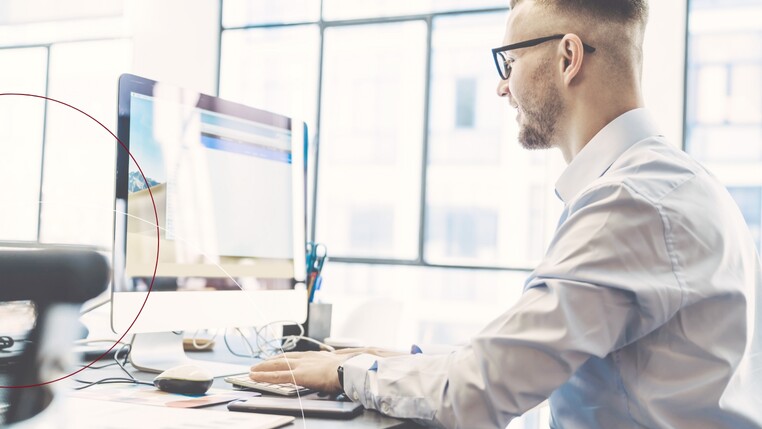 Ein Mann mit schwarzer Brille und Hemd sitzt an einem Schreibtisch