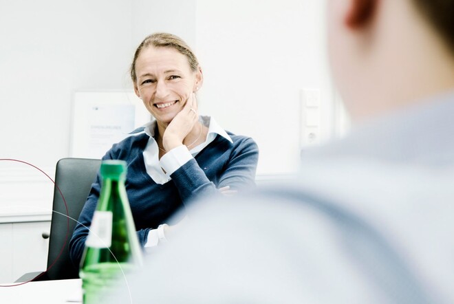 Zu sehen ist eine Frau am Schreibtisch, die sich in einem Beratungsgespräch mit einem Mann befindet.