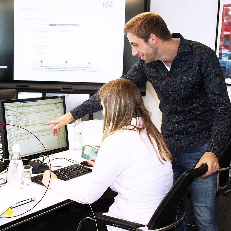 Ein Mann erklärt einer Azubin etwas am Computer