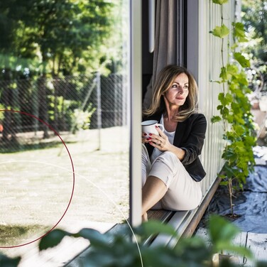 Frau mit Kaffeetasse sitzt an einer Gartentür