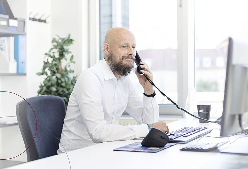 Ein Mann sitzt an seinem Schreibtisch und telefoniert.