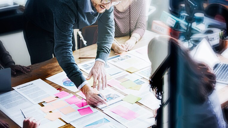 Menschen an einem Tisch, auf dem Papiere und Klebezettel liegen