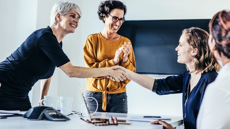 Bild mit vier Personen, zwei davon schütteln sich die Hände