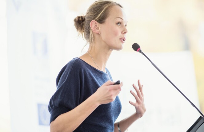 Rechteckiges Bild von einer Frau die einen Vortrag am Podest hält