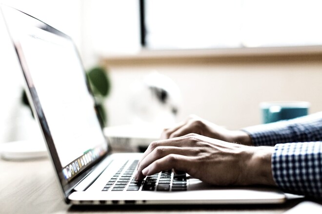 Mann im karierten Hemd schreibt am Laptop