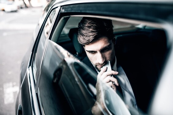 Mann mit Smartphone auf dem Rücksitz eines Autos