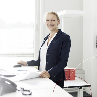 Eine ttplerin steht an einem Schreibtisch und lächelt in die Kamera