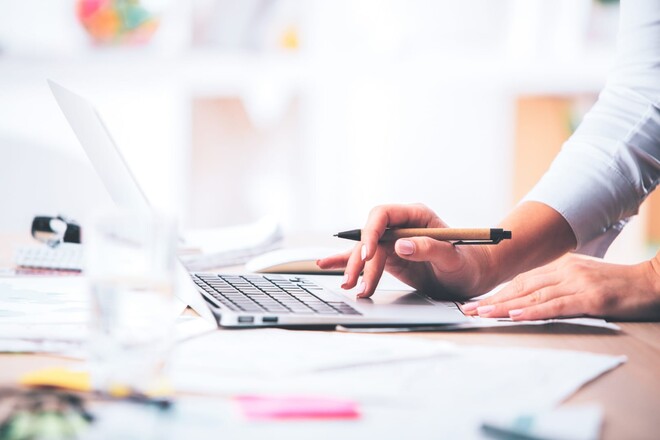 Hände, die auf einem Laptop tippen und einen Stift halten