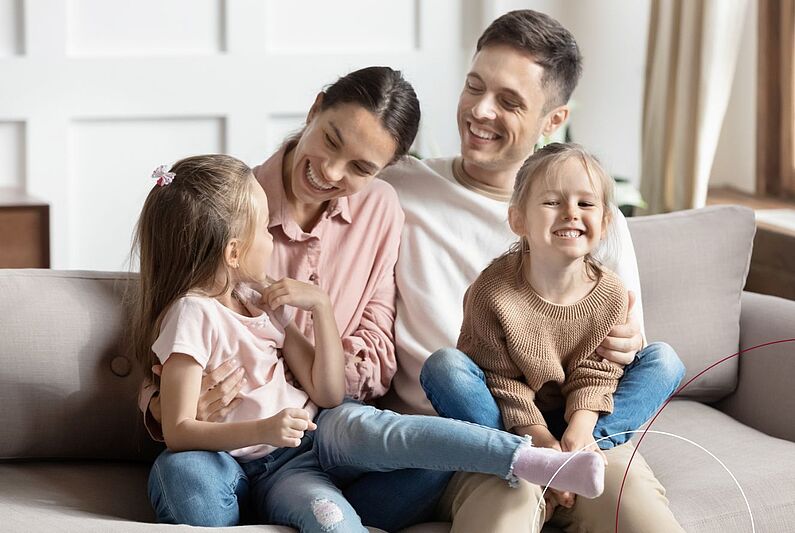 Zu sehen ist eine Familie mit zwei Mädchen, die auf einem Sofa sitzen.