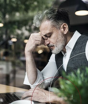 Mann sitzt vor einem Laptop und stützt seinen Kopf mit der Hand