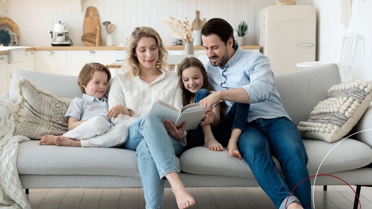 Zu sehen ist eine Familie auf einem Sofa, die sich zusammen ein Buch ansehen.