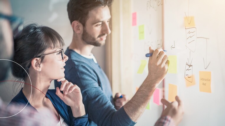Ein junger Mann und eine junge Frau beim Brainstorming an einem Whiteboard