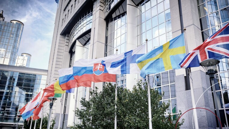 Flaggen unterschiedlicher Länder vor einer Hochhauskulisse.