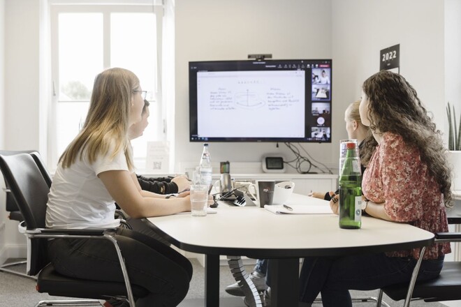 Zwei Frauen sitzen an einem Tisch und gucken auf einen Bildschirm