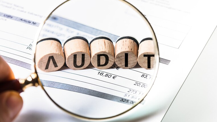 Eine Lupe vergrößert fünf auf Holz gemalte Buchstaben