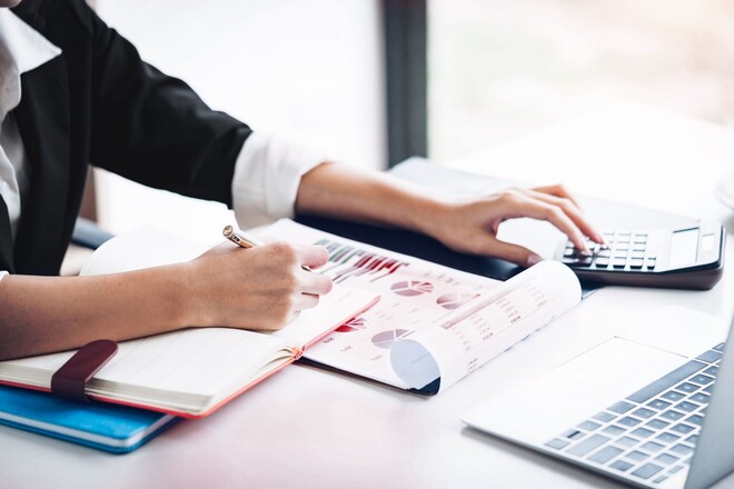Hände schreiben in ein Notizbuch und tippen auf einem Taschenrechner