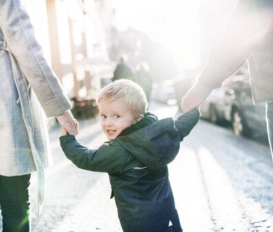Quadratisches Bild von einem Kind das die Hände seiner Eltern hält