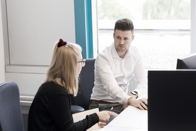 Mann und Frau sitzen am Schreibtisch nebeneinander und unterhalten sich