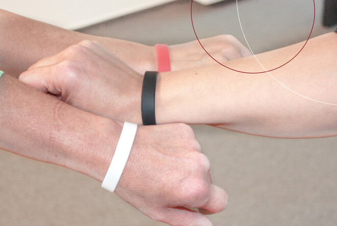 Drei Personen halten ihre Armbänder in die Kamera