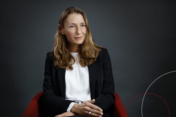 Rechteckiges Bild von sitzender Beate Theede vor schwarzem Hintergrund