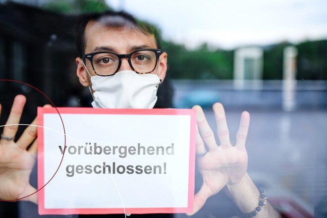 Mann klebt ein Schild ins Fenster, auf dem "Vorübergehend geschlossen" steht