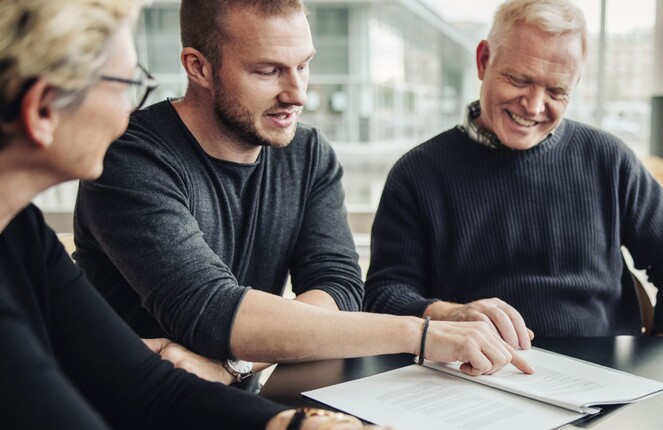 Rechteckiges Bild von drei Personen die sich ein Papier angucken