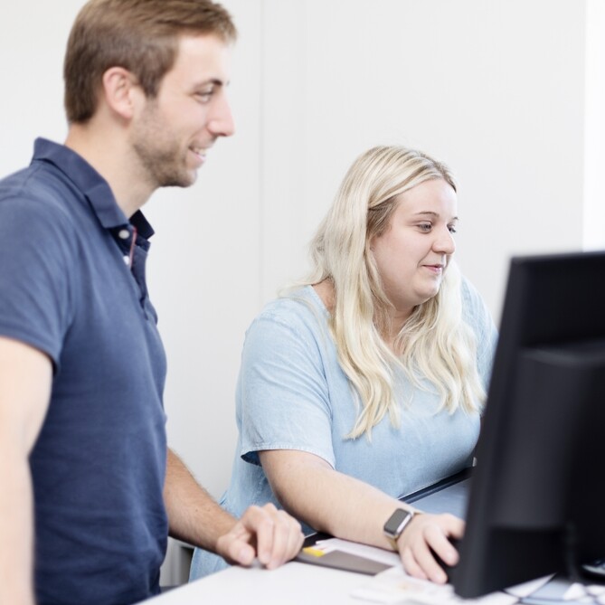 Zwei ttp Mitarbeiter stehen vor einem PC
