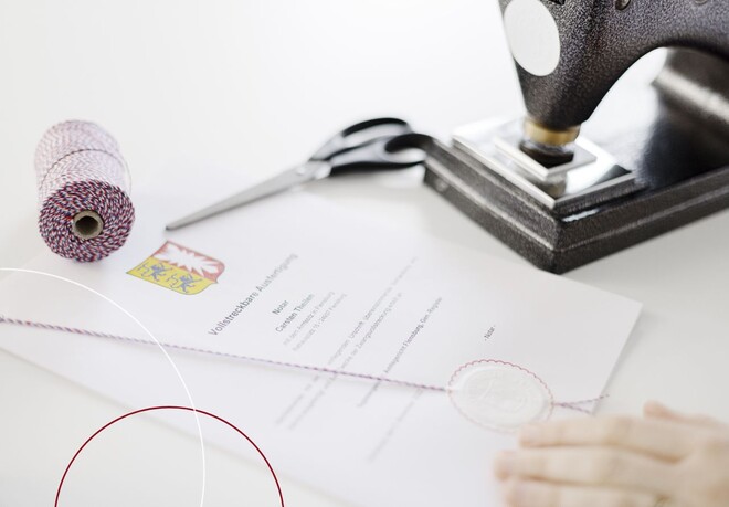 Zu sehen ist ein Gutachten, welches gerade mit einer Prägemaschine geprägt und der offiziellen Schnur versehen wurde.