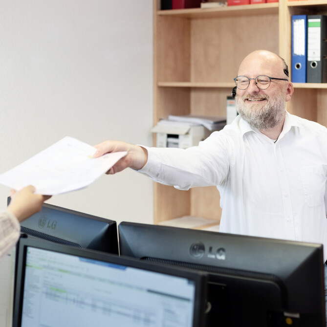 Ein ttp Mitarbeiter reicht einer Kollegin ein Stück Papier