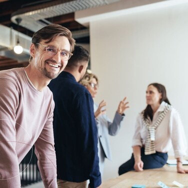Lächelnder Mann mit Brille und weitere Personen im quadratischen Zuschnitt