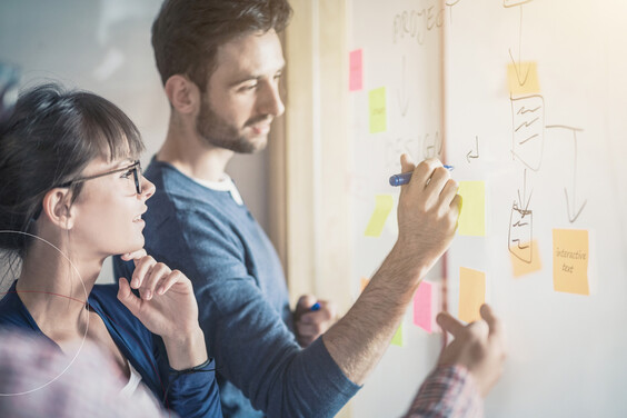 Ein junger Mann und eine junge Frau beim Brainstorming an einem Whiteboard