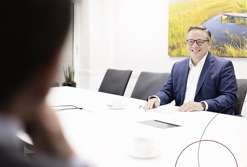 Ein Mann sitzt an einem Konferenztisch und lächelt.