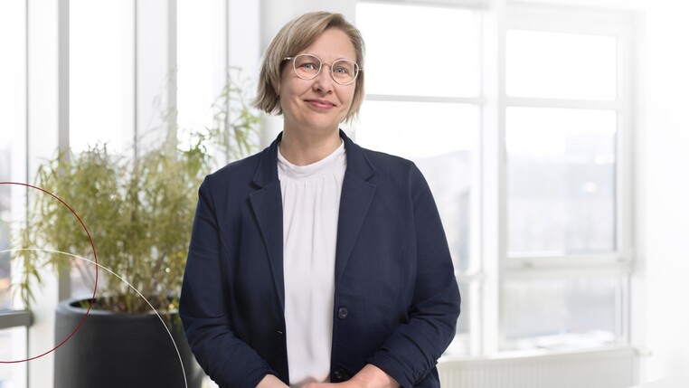 Kollegin Inga Bauch steht in ihrem Büro und lächelt in die Kamera.