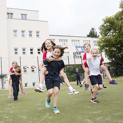 Kinder tragen sich gegenseitig auf dem Rücken und rennen über eine Wiese.
