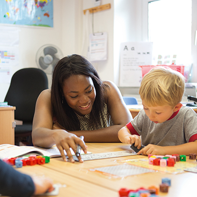 Eine Frau spielt in der Kita mit einem Kind am Tisch.